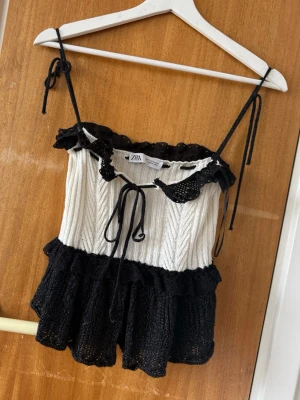 Svart och vit linnetopp från Zara - Säljer en söt linnetopp från Zara i svart och vit med volangdetaljer och knytband framtill. 