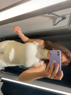 Zara Vit ribbad ärmlös polotopp - Snygg vit polotopp med ribbad struktur och spetsdetaljer vid axlarna. Toppen är ärmlös och har en tight passform som framhäver figuren. Perfekt att styla med både jeans och kjol för en trendig look.