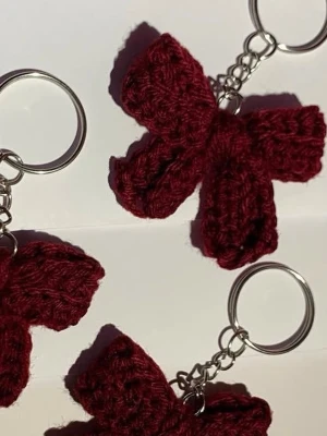 Handgjord vinröd rosett-nyckelring - Säljer en handgjord nyckelring med en vinröd virkad rosett. Rosetten är gjord av garn och sitter fast på en silverfärgad metallring. Perfekt som accessoar till väskan eller nycklarna.
