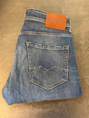 Blå jeans Replay Rocco W32/L33 - Snygga blå jeans från Replay med klassisk femficksmodell och raka ben. Jeansen har en ljus tvätt med subtila slitningar och detaljerad bakficka. Tillverkade i mjukt denimtyg för en bekväm känsla. Perfekta för en avslappnad och trendig stil.