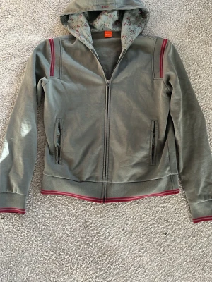 Boss zip hoodie - Säljer en skit snygg grön Hugo boss zip hoodie med ”Marseille 1927” tryck på ryggen och blomster tryck i luvan, skulle säga att den gränsar mellan s och xs