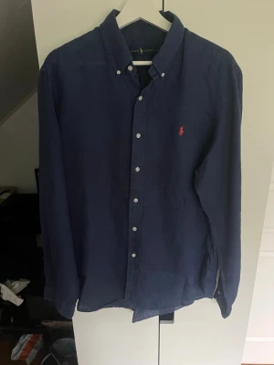 Marinblå linne skjorta från Ralph Lauren - Sjukt snygg linneskjorta från Ralph Lauren. Strl L. Mycket bra skick. Skicka gärna prisförslag. Kika in min profil för mer schyssta plagg.