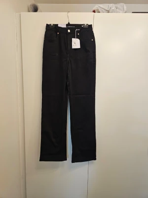 Svarta high wide jeans från JDY - Snygga svarta jeans från JDY i modellen High Wide med hög midja och raka, vida ben. Klassisk femficksdesign och silverfärgade detaljer. Perfekta för dig som gillar en trendig och avslappnad look.