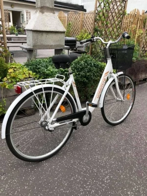 Vit Yosemite damcykel  - Säljer en vit damcykel från Yosemite med klassisk ram, svart sadel och handtag. Cykeln har en praktisk svart korg fram och pakethållare bak. Utrustad med reflexer, stänkskärmar och kedjeskydd. Perfekt för smidiga vardagsresor i stan. Broms fram och bak. 