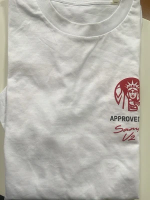 Vit t-shirt Classic V2 med tryck - Vit t-shirt med rött tryck på bröstet och stort motiv på ryggen med hamburgare, pommes och läsk samt texten 'CLASSIC V2'. Rund halsringning och avslappnad passform. Perfekt för dig som gillar streetwear och coola prints.