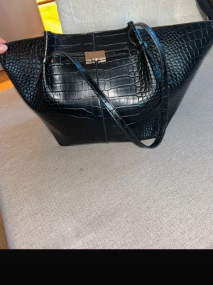 Svart Väska  - Svart väska från Lindex. Den har en liten fläck som man ser på sista bilden, men annars är den är bra skick! OBS! När man köper väskan ingår en mindre väska/neccecär. Denna ingår inte!