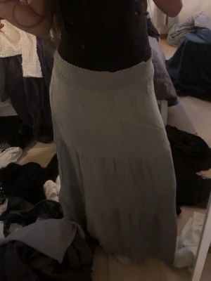 Grön långkjol med smock i midjan - Säljer en grön  långkjol med bred smock i midjan. Kjolen har en flowy passform och är perfekt för dig som gillar en avslappnad och stilren look. Materialet känns mjukt och lätt, vilket gör den skön att bära under varmare dagar.