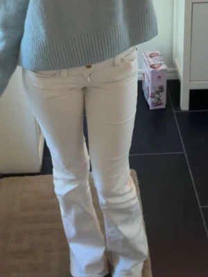 Vita bootcut jeans med låg midja - Säljer ett par vita bootcut jeans med låg midja och klassiska femficksdetaljer. Lite urtrampade längst ner, se sista bilden!  Snygg passform som sitter tajt upptill och släpper vid benen. Perfekta för en trendig och fräsch look. Storlek 26/32, modellen Bootybei från Weekday/ cheap monday!