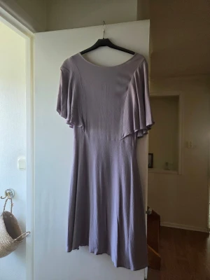 Ljuslila klänning med vida ärmar - En stilren ljuslila klänning med rund halsringning och vida, korta ärmar. Klänningen har en mjuk, lätt struktur och faller snyggt längs kroppen. Perfekt för dig som gillar en enkel men elegant look. Använd en gång på dop.