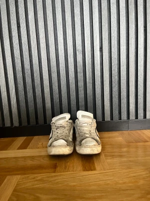 Vita sneakers med svart detalj. Philip model  - Säljer ett par vita sneakers med svarta detaljer på hälen och grå inslag. Klassisk låg modell med snörning och perforerade sidor. Skorna har en avslappnad vibe och passar perfekt till streetwear eller casual outfits.