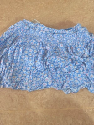 Blommiga blå shorts med resårmidja - Säljer ett par blå shorts med blommigt mönster i vitt, rosa och gult. Shortsen har en bekväm resårmidja och är gjorda i ett lätt och luftigt material, perfekta för varma dagar. Passar dig som gillar färgglada och somriga plagg!