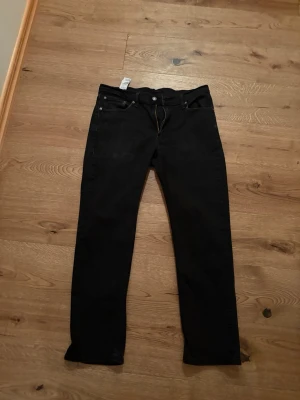 Svarta raka jeans från Levi's - Säljer ett par klassiska svarta jeans från Levi's med rak passform och fem fickor. Jeansen har en enkel design med knappgylf och bälteshällor. Perfekta till vardags för en clean och stilren look.