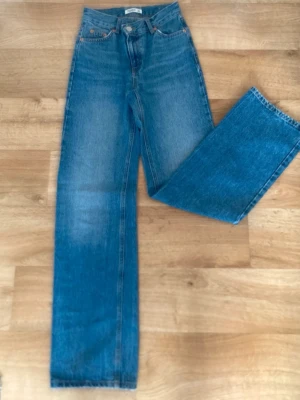 Jeans - Säljer ett par klassiska blå jeans med hög midja och raka ben. Jeansen har fem fickor, knappgylf och är tillverkade i ett slitstarkt denimtyg. Perfekta för en avslappnad och trendig look.