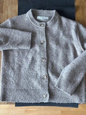 Beige kofta från Zara med knappar - Mysig beige kofta från Zara med rund halsringning och stora knappar framtill. Koftan är stickad i mjukt material och har ribbade muddar vid ärmslut och nederkant. Perfekt för lager på lager och enkel att matcha med olika outfits.