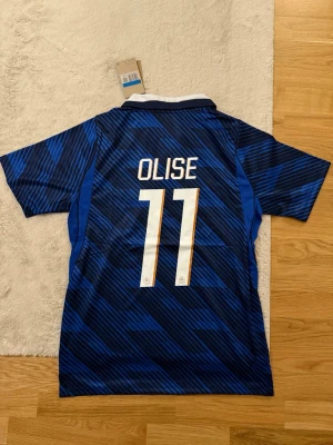 Frankrike fotbollströja Olise #11 - Snygg blå och svartmönstrad Frankrike fotbollströja från Nike med vit krage och guldiga detaljer. Nummer 11 och namnet Olise på ryggen. Tröjan har korta ärmar och FFF-emblem på bröstet. Perfekt för fotbollsfans!