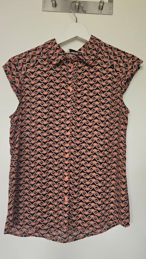 Mönstrad kortärmad blus med krage - Snygg blus med grafiskt mönster. Blusen har klassisk krage, knäppning framtill och korta ärmar. Lätt och luftig modell som passar perfekt till jeans eller kjol. Använd ett fåtal gånger.
