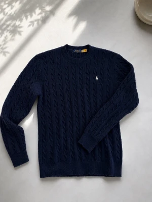 Mörkblå kabelstickad tröja Polo Ralph Lauren - Mörkblå tröja från Polo Ralph Lauren med rund halsringning och klassisk broderad logga på bröstet. Använd cirka 3 veckor påsen finns kvar som äkthet😁
