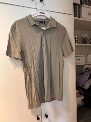 Beige kortärmad skjorta från Selected - Stilren beige skjorta från Selected med korta ärmar och klassisk krage. Skjortan har knappar framtill och är tillverkad i mjuk bomull, perfekt för en avslappnad look.