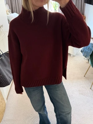 Vinröd polotröja i stickat - Mysig vinröd stickad polotröja med hög krage och avslappnad passform. Tröjan har långa ärmar och ribbade muddar vid ärmslut och nederkant. 