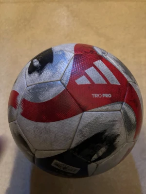 Adidas Tiro Pro fotboll - Säljer en Adidas Tiro Pro fotboll i vitt, rött och svart. Bollen har FIFA Quality Pro-märkning och är designad med moderna grafiska mönster. Perfekt för matcher och träning på hög nivå.
