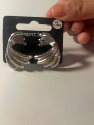 Silvriga örhängen från Montini - Snygga silvriga örhängen från Montini med vågformad design. Örhängena har en modern och stilren look som ger en cool touch till din outfit. Tillverkade i metall med blank finish. Perfekta för dig som gillar statement-smycken.