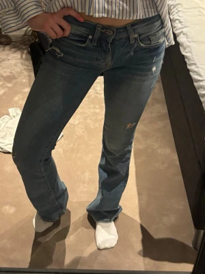 Blå bootcut jeans med slitningar - Säljer ett par blå bootcut jeans med coola slitningar och lätt utsvängda ben. Jeansen har klassisk femficksdesign och låg midja. Dem är köpta i lasvegas, gillar dem så mycket men tyvärr lite för små för mig. Köpte för 1000kr nypris. Passar mig perfekt i längden och är 160cm 