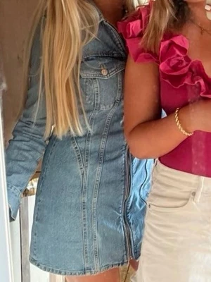 Jeansklänning med dragkedja från Zara - Snygg kort jeansklänning från Zara i blå denim med långa ärmar och hel dragkedja framtill. Klänningen har klassisk skjortkrage och två bröstfickor med knappar. Perfekt för en trendig och avslappnad look.