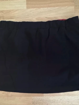 Ny Svart träning kortkjol  med innerbyxaresårmidja - En träning svart kortkjol med innerbyxa och resår i midjan. Kjolen har en rak passform och är tillverkad i ett mjukt tyg som känns bekvämt. Perfekt att matcha med olika toppar för en stilren look.
