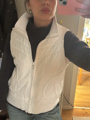 Vit dunväst från disel  - Snygg vit dunväst med dragkedja framtill och hög ribbad krage. Västen har två fickor på sidorna och bred ribbad mudd nedtill för en schysst passform. Perfekt att slänga över en hoodie eller tröja för extra värme. Enkel och clean design utan synligt märke.