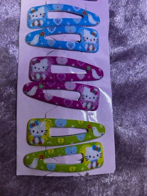 Färgglada hårspännen med kattmotiv - Säljer ett set med hårspännen i blått, rosa och grönt med söta kattmotiv och hjärtan. Spännena har glittriga detaljer och är tillverkade i metall med lackad yta. Perfekta för att piffa upp frisyren med en lekfull touch. 48kr/ 3 par / bild 