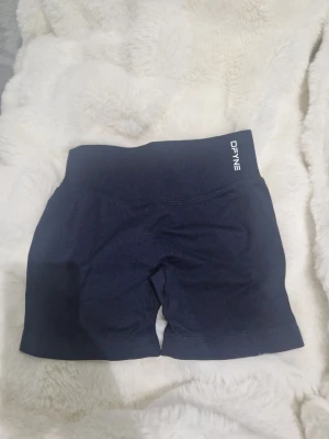 Svarta träningstights shorts från DFYNE - Säljer ett par svarta, högmidjade träningstights shorts från DFYNE. De har en tight passform och är tillverkade i ett stretchigt syntetmaterial som passar perfekt för gym eller annan träning. Diskret logga på linningen och bekväm design.