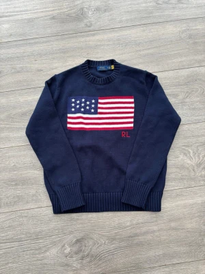 Stickad Ralph Lauren tröja - Snygg mörkblå stickad tröja från Polo Ralph Lauren med amerikansk flagga i rött, vitt och blått på bröstet samt RL-broderi. Tröjan har rund halsringning och ribbade muddar vid ärmslut och nederkant. Perfekt för dig som gillar klassisk preppy stil. Storlek S kanske något lite liten i storleken men inget jätte märkvärdigt. Bra skick, legat i garderoben länge så säljer. 