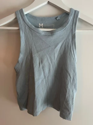 Ljusblå ribbad linnetopp - Snygg ljusblå ribbad linnetopp med breda axelband och rund halsringning. Toppen är ärmlös och har en croppad passform som passar perfekt till höga jeans eller shorts. Enkel och stilren design som är lätt att matcha.