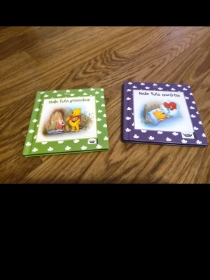 Nalle Puhs grannskap & mardröm - 50 kr styck, Två färgglada barnböcker om Nalle Puh, en grön och en lila, med illustrationer på omslagen. Båda har hårda pärmar och vita blommor runt kanterna. Perfekta för dig som gillar klassiska sagor och Disney.