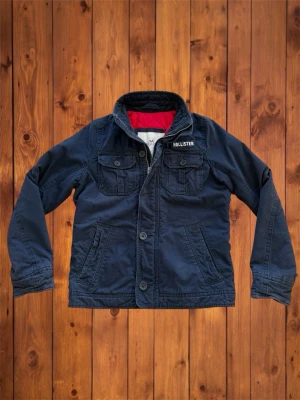Vintage Hollister Field Jacket (sällsynt) - Säljer denna vintage, sällsynta och asfeta field jackan från Hollister. Den är riktigt sällsynt och snygg och har en unik och snygg patch över bröst fickan. Den är helt perfekt jacka nu till våren istället för en vinterjacka. Storlek är M och se måtten nedan B=67cm A=55cm