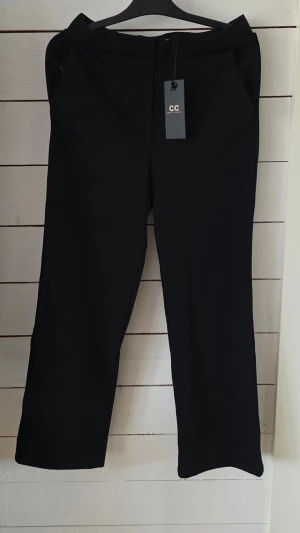 Svarta kostymbyxor från Capri Collection - Stilrena svarta kostymbyxor från Capri Collection, modell Manhattan Pants. Byxorna har raka ben och är tillverkade i en mjuk mix av 65% viskos, 30% polyester och 5% spandex för skön stretch och passform. Perfekta för en clean och modern look.