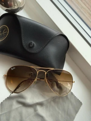 Ray-Ban aviator  - Snygga Ray-Ban aviator solglasögon med guldfärgad metallbåge och bruna tonade glas. Klassisk pilotmodell som ger en cool och tidlös look. Kommer med original svart fodral och putsduk.