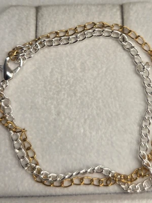 Tvåfärgat kedjearmband i rostfritt stål  - Snyggt armband med dubbla kedjor i både silver- och guldfärgad rostfritt stål. Armbandet har en klassisk karbinhake och stilren design som passar till många olika looks. Perfekt accessoar för att lyfta din outfit.