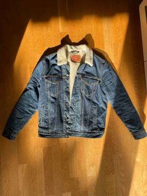 Levis Jeans Jacka Herr M - En Levis Jeans Jacka i storlek Medium. Mjukt foder mot kroppen och fodrad i armarna också. Passar bra till alla tillfällen och är bra nu på våren när det kan vara lite kyligare på morgonen fast för varmt med vinterjacka. Inga tydliga defekter och i bra skick. Kom med frågor och funderingar. 
