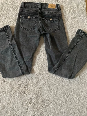 Svarta straight leg jeans Gina Tricot - Säljer ett par mörkgråa straight leg jeans från Gina Tricot, modell 'perfect jeans'. Jeansen har två bakfickor med lock och knappdetaljer samt klassisk femficksdesign. Materialet är denim i bomull med snygg tvättad look.