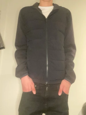 Cardigan  - Snygg svart pufferjacka med hel dragkedja framtill och diskreta sidofickor. Jackan har en enkel, stilren design med lätt vaddering och raka ärmar. Perfekt för kalla vinterdagar och passar till det mesta. Materialet känns mjukt och bekvämt.