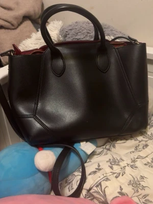 Väska - Svart väska, vinrött där man stänger och insidan av väskan svart. Skitsnygg men lite för stor för min smak. Kan få plats med mycket bra grejer i. Aldrig använt från Zara