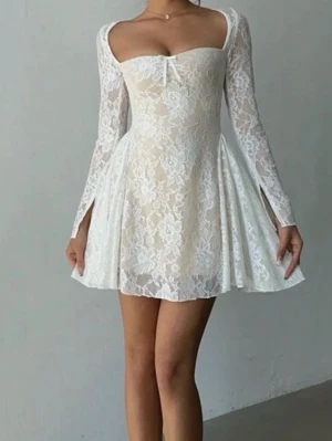 Vit spetsklänning med lång ärm - Supersöt vit kortklänning i spets med långärmade ärmar och en liten rosett framtill. Perfekt till studenten i vår eller midsommar