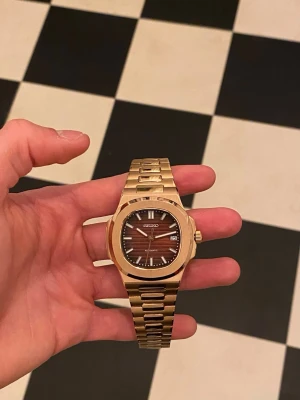 Rosegold Seiko Mod Nautilus  - Helt ny oanvänd, Seiko mod Nautilus med Automatisk Seiko-NH35-urverk. ✅  Öppen baksida (display caseback).✅  Storlek: 40mm✅  Rosegold-färgad länk och boett i rostfritt stål, reptåligt safirglas, brun urtavla med datum.✅  Medföljer klocklåda, ej original✅  Vid fler frågor eller funderingar skicka gärna ett pm, Mvh🙂