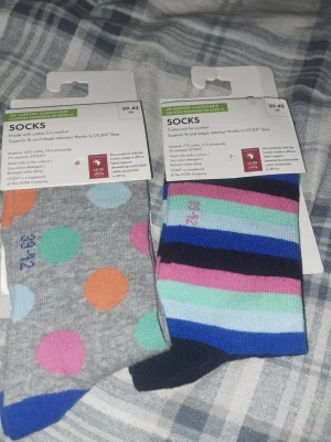 Färgglada strumpor med prickar & ränder - Två par strumpor från Carter's i storlek 39-42. Ett par är grå med stora färgglada prickar i orange, turkos, rosa och blått. Det andra paret har ränder i blått, rosa, mintgrönt och svart. Tillverkade i bomullsmix med Lycra® för extra komfort och passform.