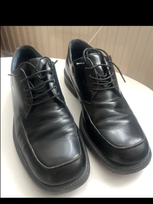 Svarta läderkängor från Björn Borg  - Stilrena svarta kängor från Björn Borg i blankt läder med fyrkantig tå och klassisk snörning. Insidan är fodrad i blått tyg och sulan är robust för extra komfort. Perfekta för dig som vill ha en clean och tidlös look.