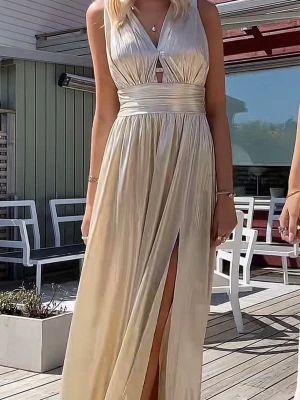 Champagnefärgad långklänning med slits - Elegant långklänning i champagnefärg med v-ringad omlottdesign och bred markerad midja. Klänningen har ärmlös modell och hög slits framtill som ger en stilren och festlig look. Materialet har en lätt glansig finish som fångar ljuset snyggt. (Lånad bild)💛💛