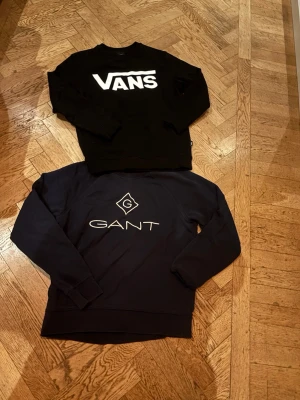 Svart Vans & marinblå Gant tröja - Två snygga sweatshirts: en svart Vans-tröja med stor vit logga på bröstet och en marinblå Gant-tröja med vit logga och emblem framtill. Båda har klassisk passform och långa ärmar, perfekta till jeans eller joggers. 100kr styck.
