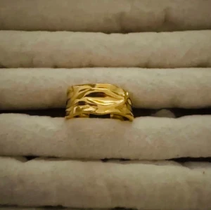 Bred guldfärgad ring med vågig yta - Snygg bred ring i guldfärg med vågig, strukturerad yta som ger en cool och unik look. Ringen har en blank finish och passar perfekt för dig som vill sticka ut med dina accessoarer. Ingen synlig märkning.