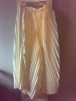 Nike byxor  - Säljer en elegant vit långbyxor med plisserad design och bred midja med snörning. Kjolen har ett luftigt fall och passar perfekt till både sneakers och boots. Materialet känns lätt och flowy, vilket gör den superbekväm att bära. Nypris 1949 